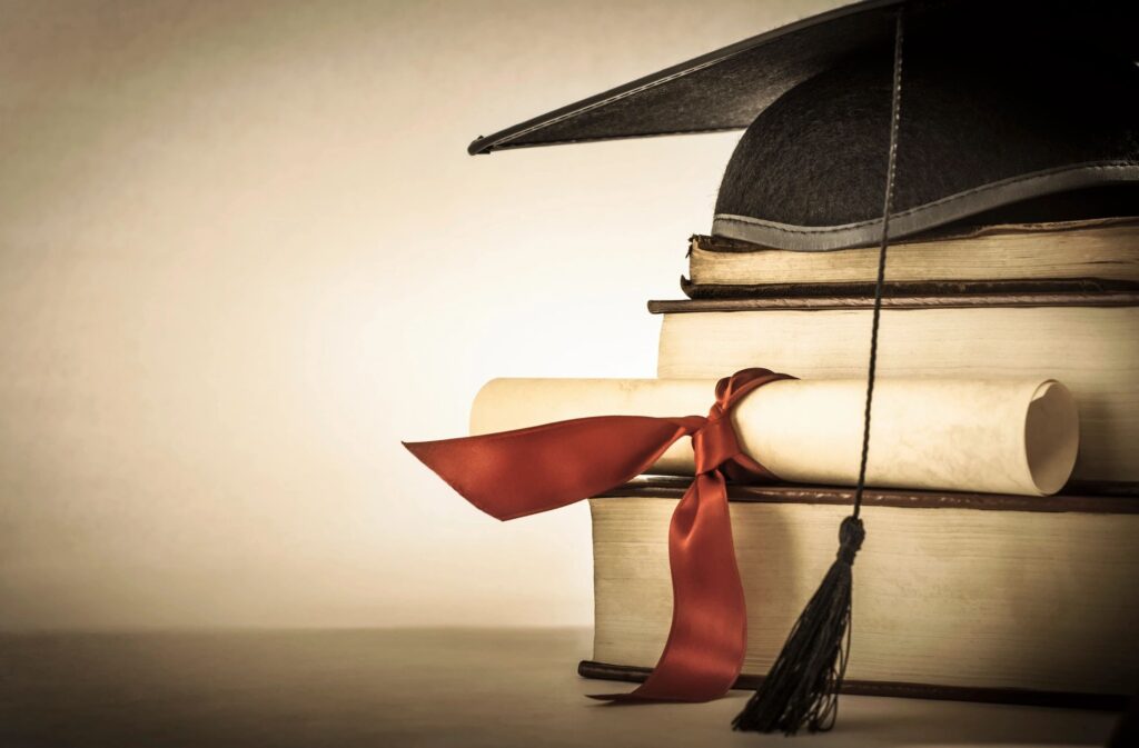 A stack of books with a red ribbon and a cap on top.